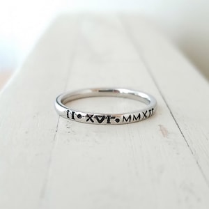 May include: A silver band ring with the inscription "II.XVI.MMXI" engraved on the outside.