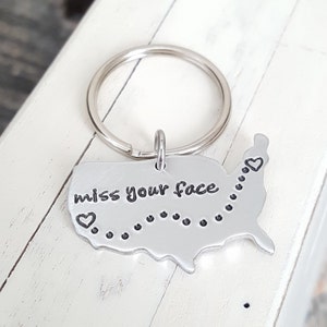 May include: Silver keychain with a map of the United States and the text "miss your face" with a heart on each side of the text.