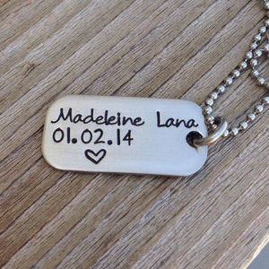 May include: Silver dog tag necklace with a personalised inscription that reads "Madeleine Lana 01.02.14" with a small heart symbol.
