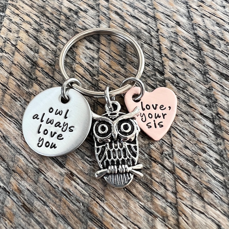 Pode incluir: Um chaveiro com um charme de coruja prateada, um charme redondo prateado que diz "owl always love you" e um charme de cora&ccedil;&atilde;o de cobre que diz "love, your sis".