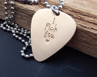 May include: A silver chain necklace with a gold-colored guitar pick pendant. The pick has the words "I pick you" engraved on it with a small heart.