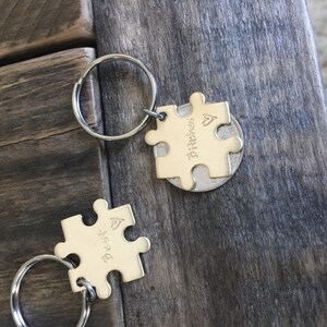 May include: Two gold-toned puzzle piece keychains with a heart symbol and the words "Bitches" and "Best" engraved on them. The keychains are attached to silver key rings.