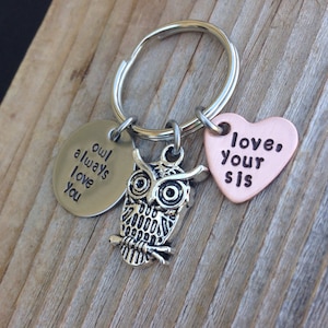 Pode incluir: Um chaveiro com um charme de coruja prateada, um charme prateado que diz "owl always love you" e um charme de cora&ccedil;&atilde;o de cobre que diz "love your sis".