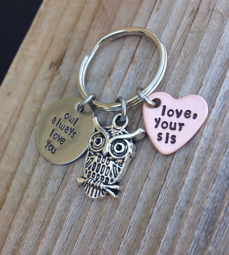 Pode incluir: Um chaveiro com um charme de coruja prateada, um charme prateado que diz "owl always love you" e um charme de cora&ccedil;&atilde;o de cobre que diz "love your sis".