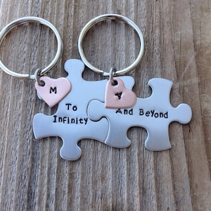May include: Two silver puzzle pieces with key rings, each with a small heart charm. The left piece says "To Infinity" and the right piece says "And Beyond". The hearts are copper and have the letters "M" and "Y" engraved on them.