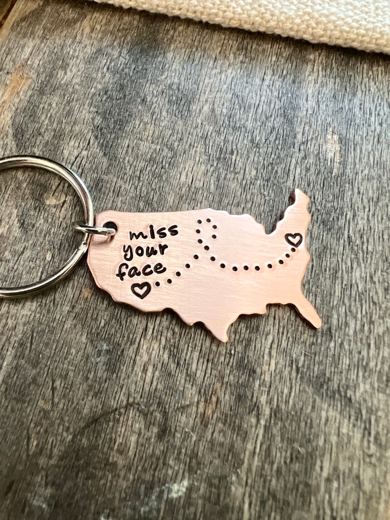 May include: A copper-colored keychain shaped like the United States with the words "miss your face" and a dotted line across the country. There are three small hearts on the keychain.