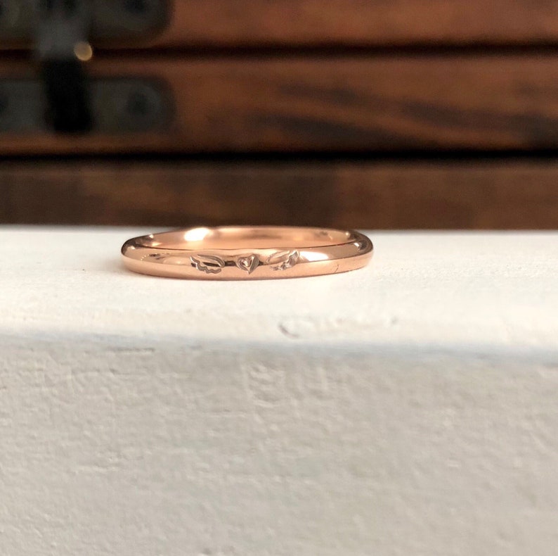 Peut inclure: Une fine bague en or rose avec un c&oelig;ur et deux ailes grav&eacute;s sur la surface.