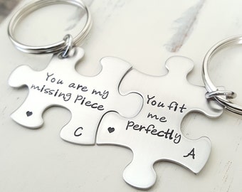 May include: Two silver puzzle piece keychains with the text "You are my missing piece" and "You fit me perfectly" on them. The keychains are connected together.