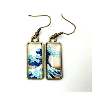 Puede incluir: Un par de pendientes de bronce con paneles de vidrio rectangulares que presentan una impresión de la Gran Ola de Kanagawa de Hokusai. Los pendientes tienen un cierre de gancho.