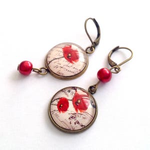 May include: A pair of earrings with red poppy flower designs on round glass cabochons. The earrings have bronze-colored metal hooks and red bead accents.