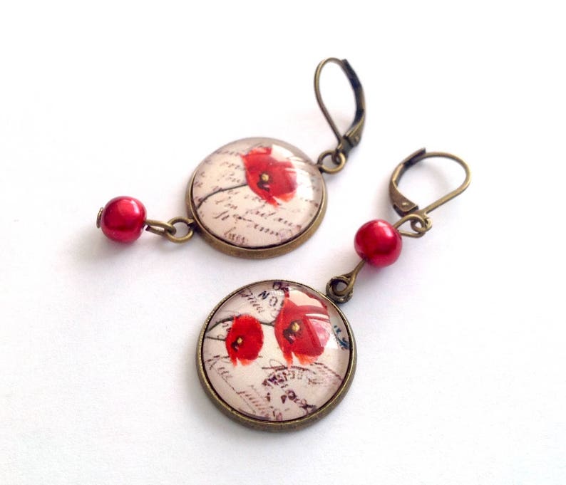May include: A pair of earrings with red poppy flower designs on round glass cabochons. The earrings have bronze-colored metal hooks and red bead accents.