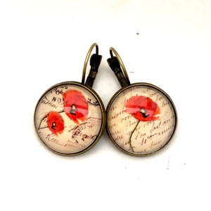 May include: A pair of bronze hoop earrings with a round glass charm featuring a vintage postcard image of red poppies on a cream background with handwritten French text.