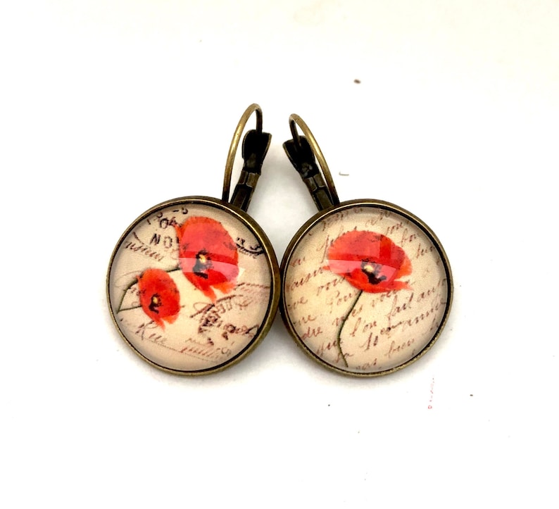 May include: A pair of bronze hoop earrings with a round glass charm featuring a vintage postcard image of red poppies on a cream background with handwritten French text.