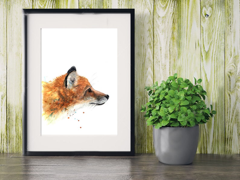 May include: A watercolour painting of a red fox's head and shoulders, looking to the right. The fox is painted in shades of orange, brown, and white, with a few splashes of colour around it. The painting is framed in a black frame and is displayed on a wooden surface.