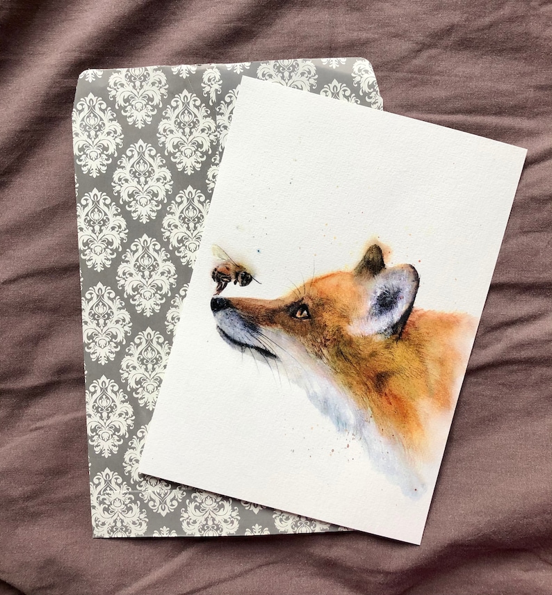 May include: A watercolour painting of a fox with a bee flying in front of its nose. The fox is looking at the bee with a curious expression. The painting is done in shades of brown, orange, and yellow.