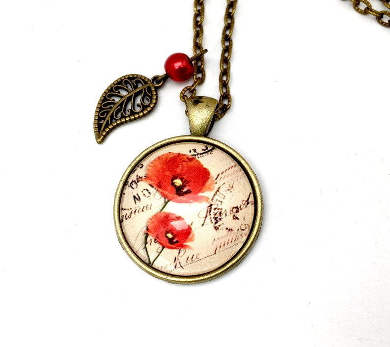 May include: A bronze necklace with a round pendant featuring a vintage postcard image of red poppies. The pendant is attached to a bronze chain with a small bronze leaf charm and a red bead.