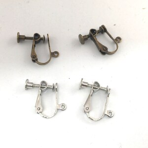 May include: Two pairs of earring clips, one pair is silver and the other is bronze. The clips are designed to hold earrings in place.