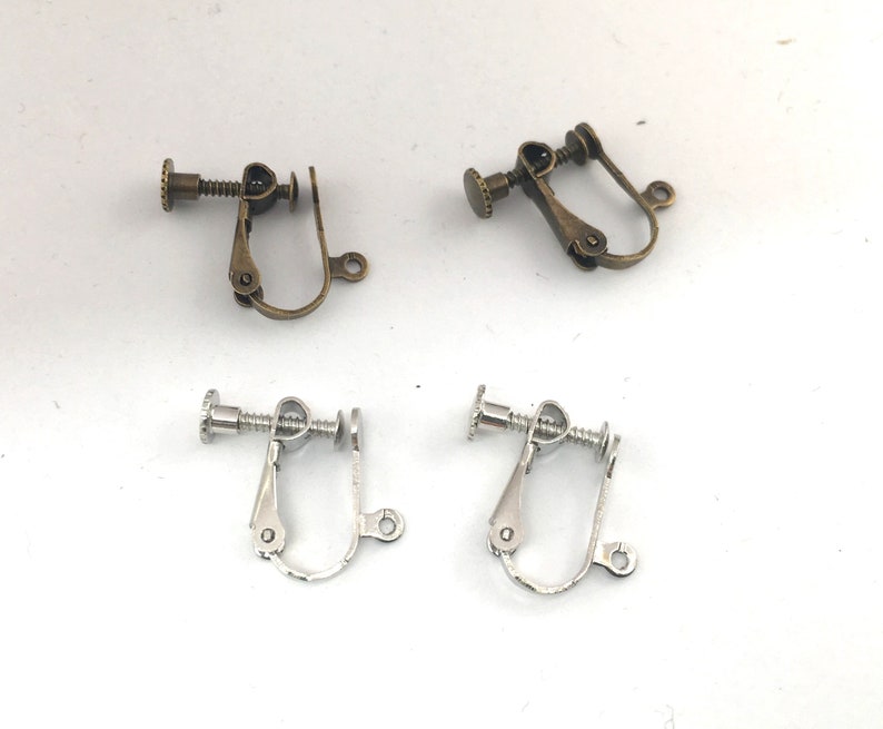 May include: Two pairs of earring clips, one pair is silver and the other is bronze. The clips are designed to hold earrings in place.
