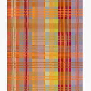 Puede incluir: Un textil tejido colorido con un patrón de cuadros. El diseño presenta líneas verticales y horizontales en tonos de naranja, amarillo, rosa y morado. El textil es rectangular y parece ser un artículo decorativo.