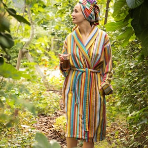 May include: A multi-coloured striped bathrobe featuring a shawl collar, long sleeves, and a matching tie belt at the waist, paired with a coordinating multi-coloured striped head wrap, both crafted from a textured fabric with vertical stripes.