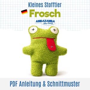 Könnte beinhalten: Ein grünes, strukturiertes Stofftier in Froschform mit zwei weißen Knopfaugen mit schwarzer Kreuzstickerei, einer geraden roten Mundlinie und einer herausragenden roten Zunge. Der Text lautet Kleines Stofftier Frosch AMBAZAMBA sew funny PDF Anleitung & Schnittmuster.