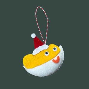 Peut inclure: Ornement de Noël fait à la main en forme de poisson-globe jaune, coiffé d'un bonnet de Père Noël rouge avec un pompon blanc. L'ornement a des détails en feutre blanc, des yeux globuleux et une bouche rouge et orange. Une ficelle rouge et blanche est attachée pour l'accrocher.