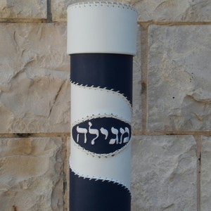 May include: A white and blue cylindrical container with a white leather cover and a white stitched oval with the Hebrew word "Megilat" in white thread.