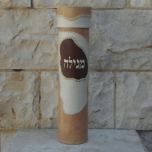 May include: A brown leather Torah scroll case with white leather accents and the Hebrew word "Megilat" written on the front.
