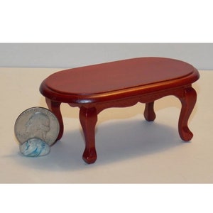 Puede incluir: Una mesa de café ovalada de madera en miniatura con cuatro patas. La mesa está hecha de madera oscura y tiene un acabado liso. La mesa es aproximadamente del tamaño de una moneda de 25 céntimos de euro.