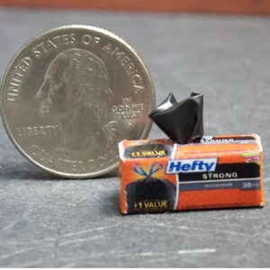 May include: A miniature box of Hefty Strong trash bags, with a black trash bag on the front of the box. The box is orange and blue with the text "Hefty Strong" and "30 Count" printed on it. A miniature US quarter is included for scale.