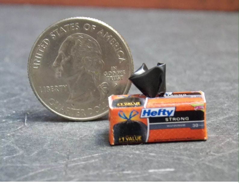 May include: A miniature box of Hefty Strong trash bags, with a black trash bag on the front of the box. The box is orange and blue with the text "Hefty Strong" and "30 Count" printed on it. A miniature US quarter is included for scale.