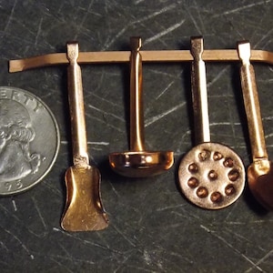 May include: Set of four miniature copper kitchen utensils hanging on a wooden rack. The utensils include a ladle, a spatula, a slotted spoon, and a small spoon.