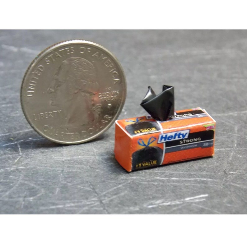 May include: A miniature box of Hefty Strong trash bags, with a black trash bag sticking out of the top. The box is orange and white with the Hefty logo and the words "Strong" and "30 Count".