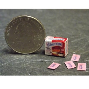 Op de afbeelding: Een miniatuurdoosje met Sweet'N Low suikervervanger, naast een Amerikaanse kwartje, en vier roze Sweet'N Low-zakjes.
