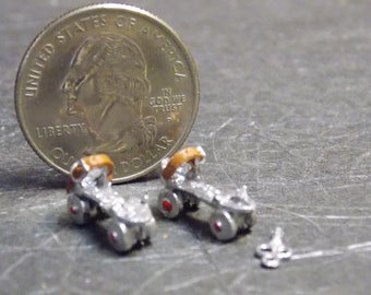May include: A pair of miniature silver roller skates with brown leather straps and red wheels. The skates are next to a US quarter dollar coin for scale.