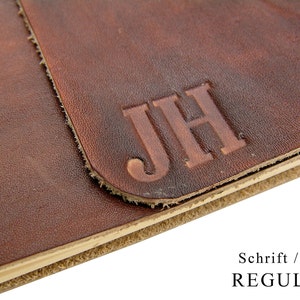 May include: Close-up of a brown leather journal with the initials "JH" embossed on the front. The journal has a cream-coloured edge.
