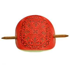 May include: Red leather hair stick with a decorative carved design and a wooden pin.