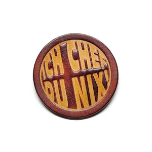 Könnte beinhalten: Ein runder, brauner Leder-Patch mit dem Text "Ich Chef Du Nix" in kontrastierendem Gelb.