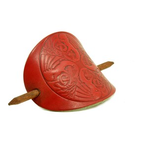Könnte beinhalten: Roter Haarstick aus Leder mit einem geschnitzten Design. Der Stick ist aus Holz und hat ein rotes Lederstück mit einem geschnitzten Design.
