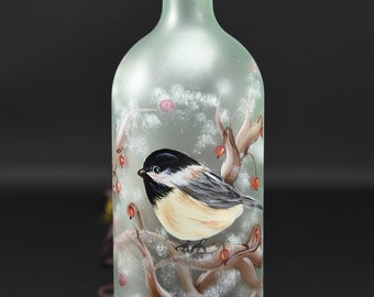 Könnte beinhalten: Eine mattierte Glasflasche mit Korken, handbemalt mit einem detaillierten Bild einer Kohlmeise, die auf einem Ast mit roten Beeren sitzt. Der Vogel hat schwarze, weiße und beige Federn. Die Flasche ist etwa 25 cm hoch.