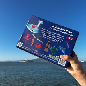 May include: Blue box with a whale, octopus, fish, seahorse, crab, turtle, and dolphin on it. The box is for a bath toy set that recreates the story of Jonah and the whale. The text on the box reads "Splash and Pray Fun with your heavenly friends!"