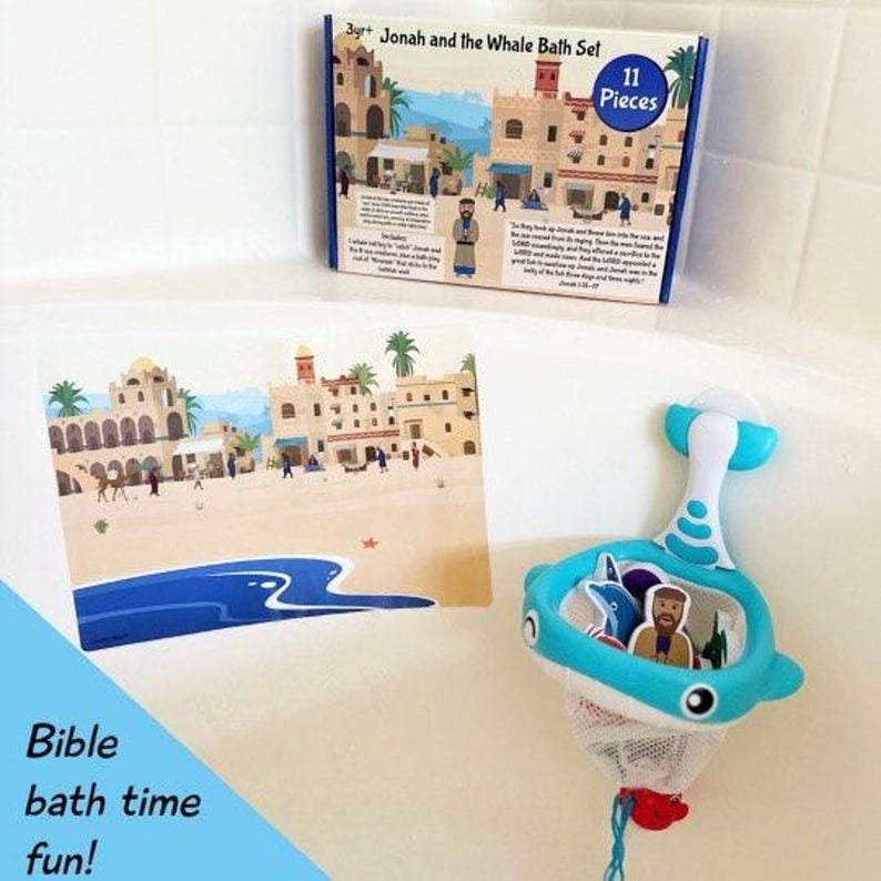 May include: A blue whale bath toy with a net for holding bath toys. The toy is on a white surface with a blue and white illustration of a beach scene and the text "Jonah and the Whale Bath Set" and "11 Pieces".