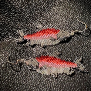 May include: A pair of beaded salmon earrings with silver hooks. The salmon are red, pink, and white with gray details.