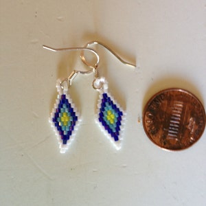 May include: A pair of beaded earrings with a diamond shape and a blue, white and yellow pattern. The earrings are hanging from silver hooks.