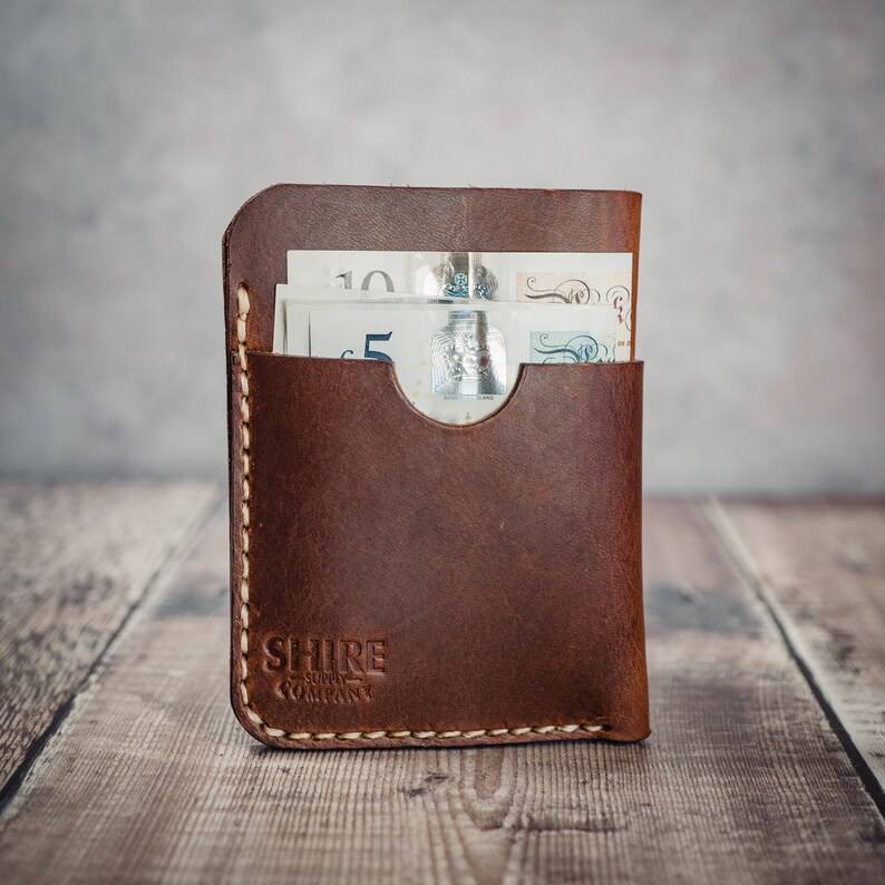 May include: A brown leather wallet with a flap and a single pocket for bills. The wallet has a stitched edge and the text "SHIRE SUPPLY COMPANY" is embossed on the front.