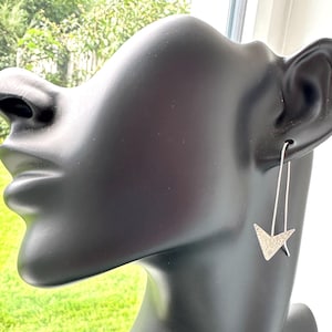 Könnte beinhalten: Silberne Ohrringe in Dreiecksform mit strukturierter Oberfläche. Die Ohrringe hängen an einem silbernen Draht.