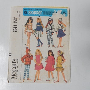 May include: A vintage McCall's sewing pattern for Barbie's Little Sister Skipper dolls. The pattern includes eight different outfits, including a red hooded jacket, a blue and white plaid skirt, a pink dress, and a yellow polka dot dress. The pattern number is 7841 and the price is 65 cents.