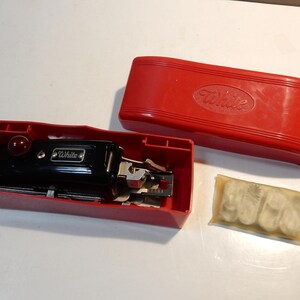 May include: A vintage black sewing machine with the "White" brand name, housed in a red case. The case is open, revealing the machine and accessories. A small packet of accessories is also present.