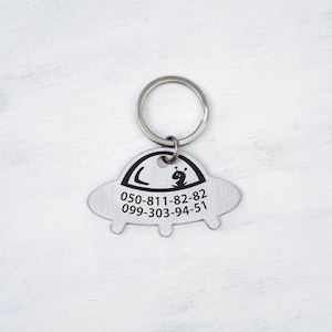 May include: Silver UFO-shaped keychain with a black alien and phone numbers 050-811-82-82 and 099-303-94-51.