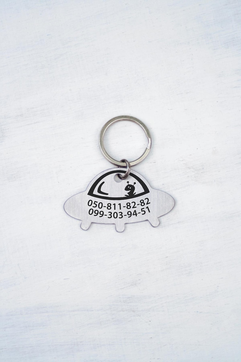 May include: Silver UFO-shaped keychain with a black alien and phone numbers 050-811-82-82 and 099-303-94-51.